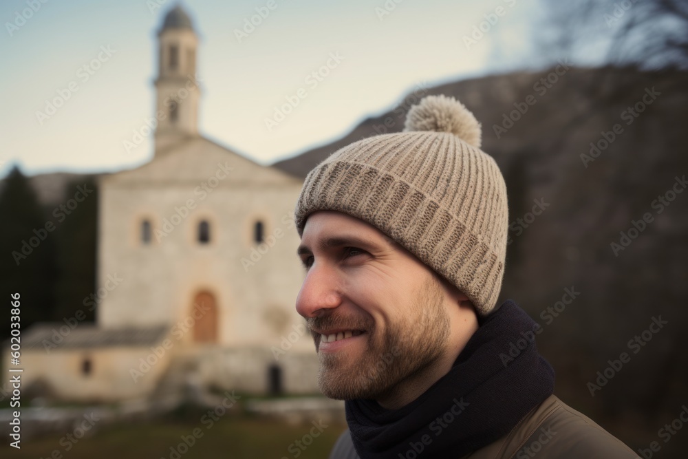 Portrait of a handsome young man in a warm hat and scarf against the background of the church Portrait of a handsome young man in a warm hat and scarf against the background of the church