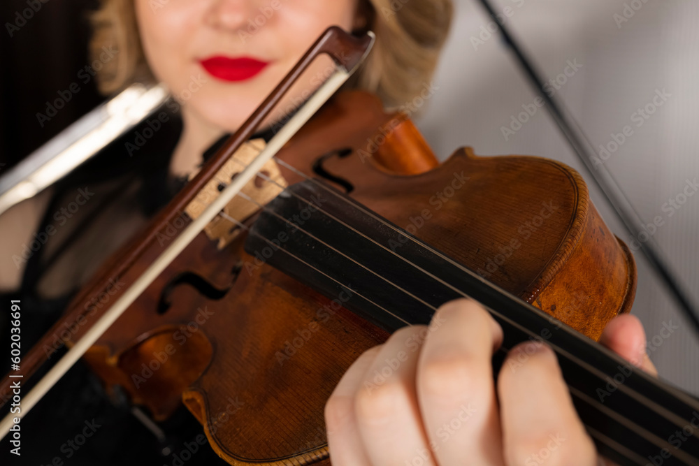 Young elegant blonde girl posing with a violin. Portrait of a female violinist playing, performing against a piano. Young elegant blonde girl posing with a violin. Portrait of a female violinist playing, performing against a piano.