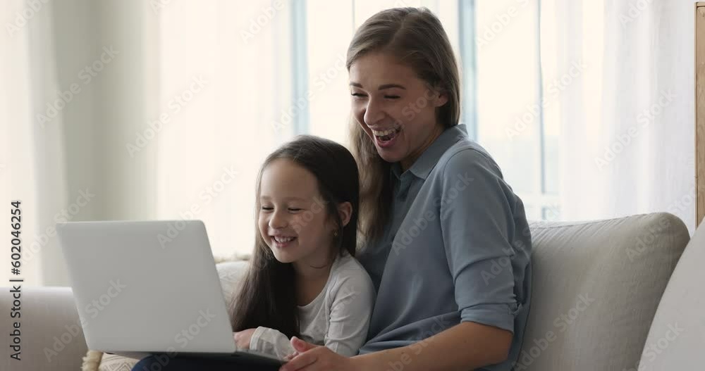 Cheerful mom holding sweet girl and laptop on lap, talking on online video call, smiling, laughing. Happy pretty young mother and kid using computer at home, watching cartoon movie on Internet Cheerful mom holding sweet girl and laptop on lap, talking on online video call, smiling, laughing. Happy pretty young mother and kid using computer at home, watching cartoon movie on Internet