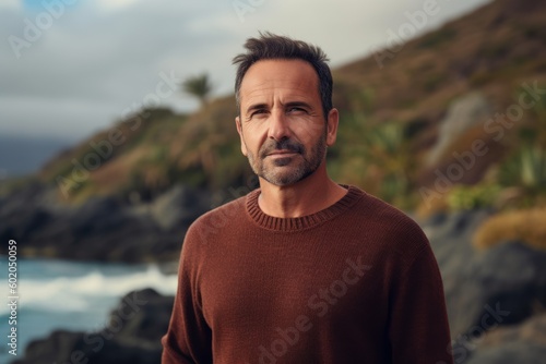 Portrait of a handsome mature man wearing a brown sweater standing by the ocean