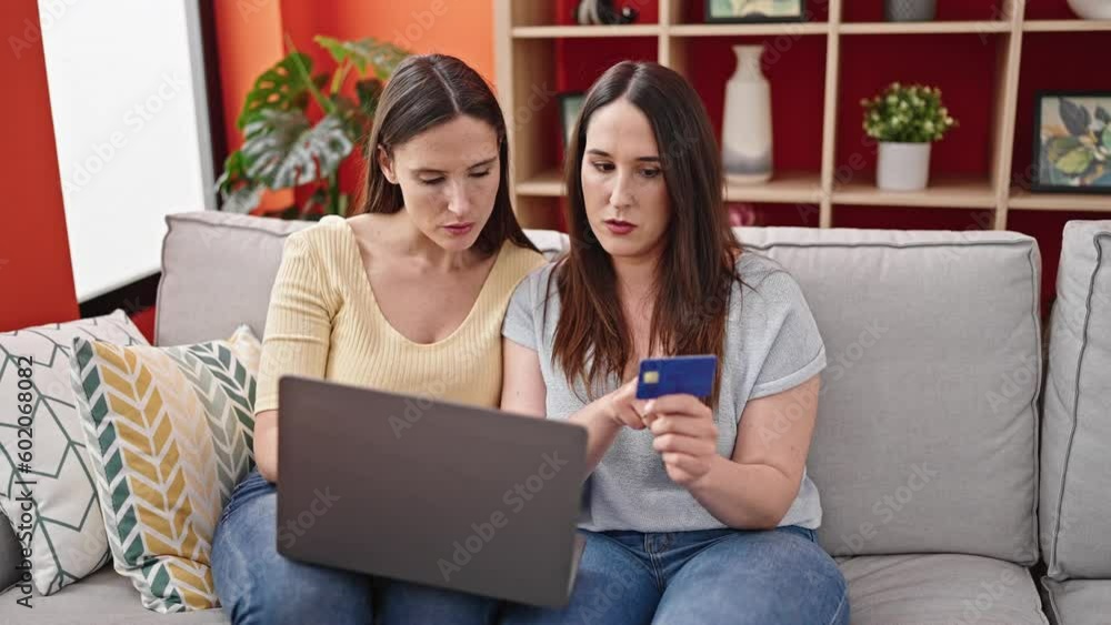 Two women sitting on sofa shopping with laptop and credit card at home Two women sitting on sofa shopping with laptop and credit card at home