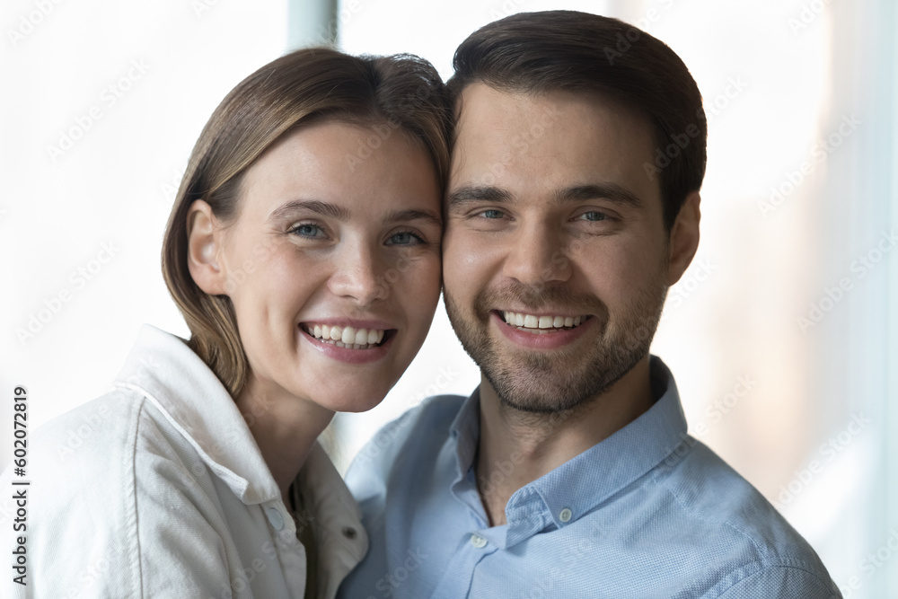 Happy young handsome husband and beautiful wife looking at camera with toothy smiles, laughing, hugging with cheek touch. Positive dating couple in love, healthy romantic relationships close portrait Happy young handsome husband and beautiful wife looking at camera with toothy smiles, laughing, hugging with cheek touch. Positive dating couple in love, healthy romantic relationships close portrait