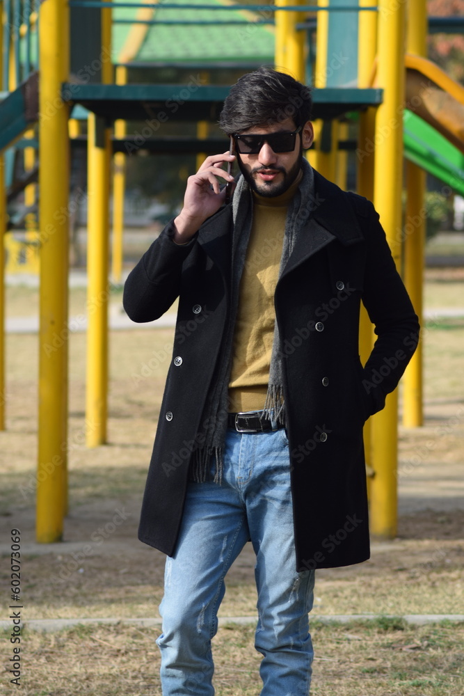 Young man talking on the phone while standing in a park Islamabad, Pakistan.