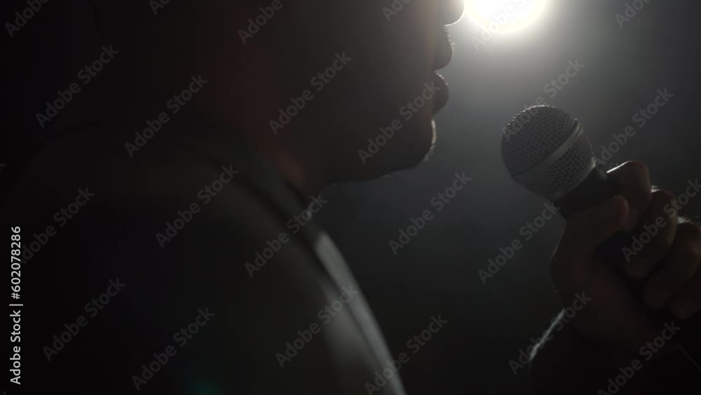 Close up shots microphone speaker man talking on stage with spotlight strike through the darkness at corporate business event. Public speaker giving talk at conference hall. Stand up comedian. Close up shots microphone speaker man talking on stage with spotlight strike through the darkness at corporate business event. Public speaker giving talk at conference hall. Stand up comedian.