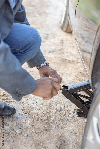 Detail of hands of a latino man changing a flat tire on his car at the side of the road.