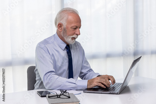 Senior businessman using laptop sitting by the desk. Confident CEO or director working in his modern office.