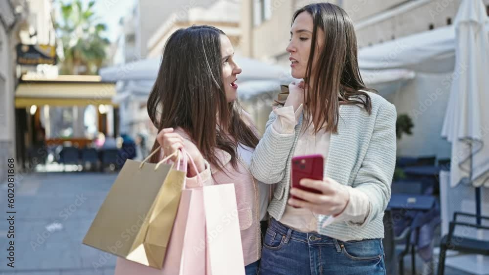 Two women going shopping holding bags using smartphone at coffee shop terrace Two women going shopping holding bags using smartphone at coffee shop terrace