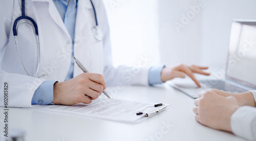 Doctor and patient discussing current health questions while sitting near of each other and using clipboard at the table in clinic, just hands closeup. Medicine concept