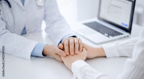 Doctor and patient sitting near each other at the table in clinic office. The focus is on female physician s hands reassuring woman  only hands  close up. Medicine concept
