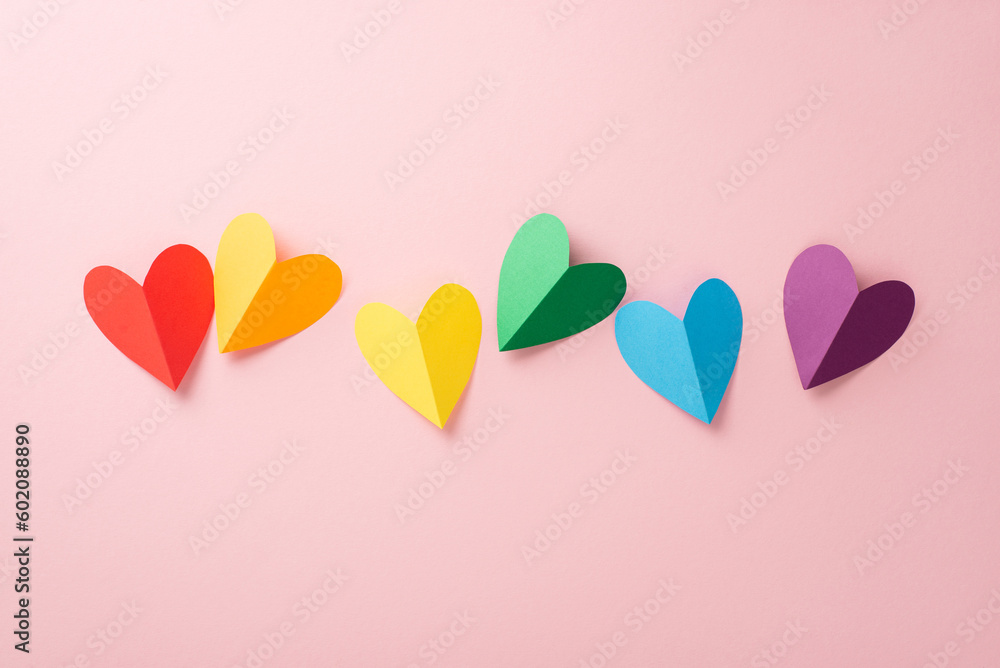 A flat lay top view of LGBT pride items: a rainbow colored paper hearts, placed on a pastel pink backdrop in line composition - obrazy, fototapety, plakaty 