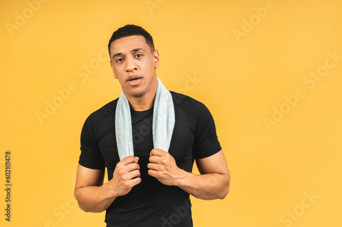 Portrait of african american male athlete after workout isolated over yellow background. Muscular man with a towel with his hands.