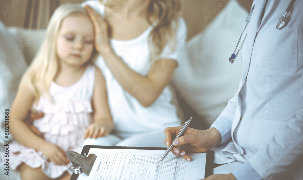 Doctor and patient. Pediatrician using clipboard while examining little girl with her mother at home. Happy cute caucasian child at medical exam. Medicine concept Doctor and patient. Pediatrician using clipboard while examining little girl with her mother at home. Happy cute caucasian child at medical exam. Medicine concept