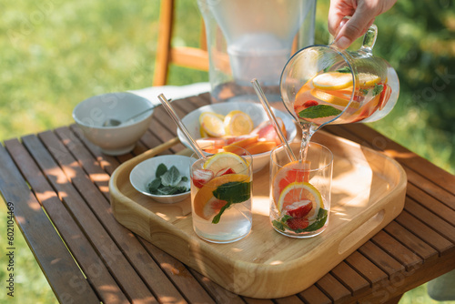 Woman pouring a glass of water with assorted fresh fruit and mint leaves in the garden photo