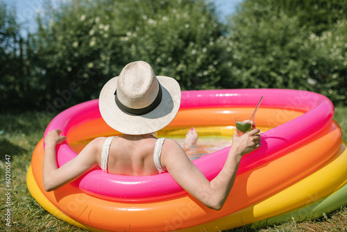Rear view of a woman sitting in a paddling pool in summer with a refreshing fruit drink photo