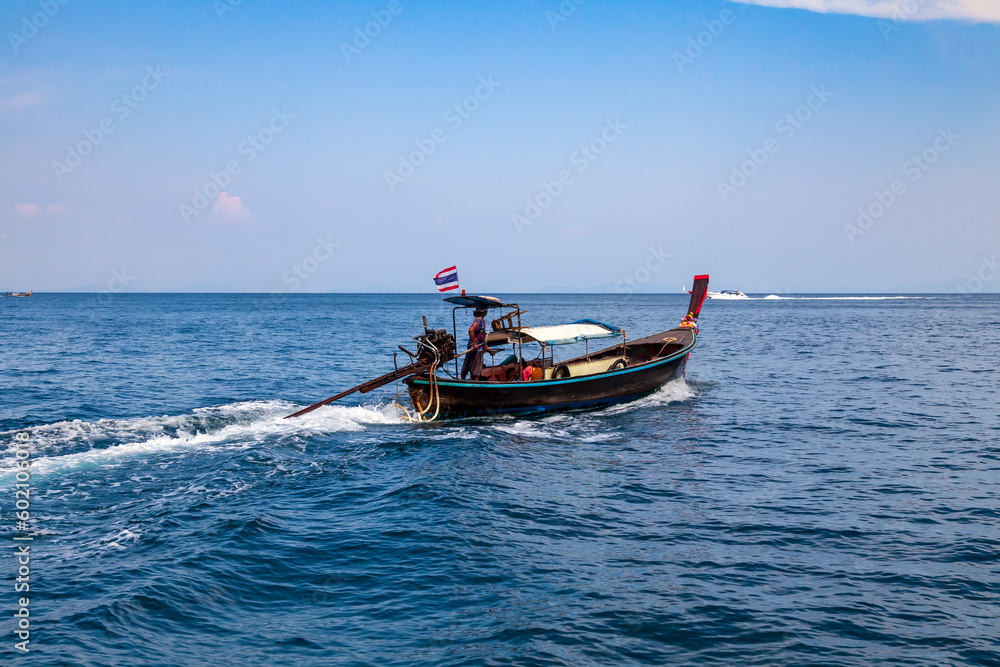 Old traditional Thai motorboat made of wood for fishing and tourists on excursions in the Andaman Sea near Phi Phi Leh island in clear turquoise water under a blue sky. Travel and vacation in phuket.