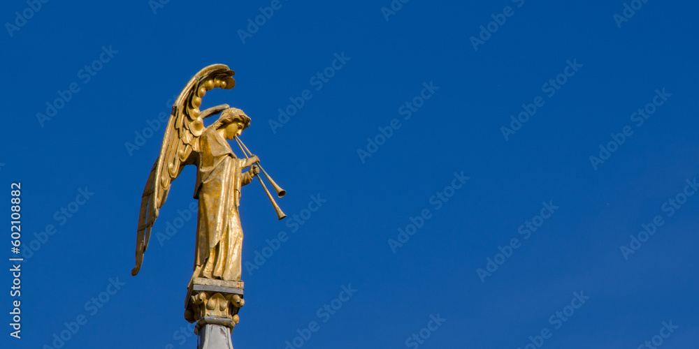 Gilded sculpture of an angel playing a pipe against a clear sky. Copy space. Statue of an angel on the top of a church column.