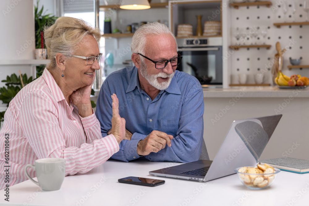 Cheerful senior couple making video call and waving hands to laptop. Elderly spouses gesturing hello to family or friends. Remote online communication Cheerful senior couple making video call and waving hands to laptop. Elderly spouses gesturing hello to family or friends. Remote online communication