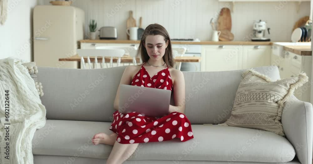Positive young adult gen Z girl in red cloth typing on laptop at home, using Internet service, app, software, browsing website, watching online video, smiling, laughing, looking away Positive young adult gen Z girl in red cloth typing on laptop at home, using Internet service, app, software, browsing website, watching online video, smiling, laughing, looking away
