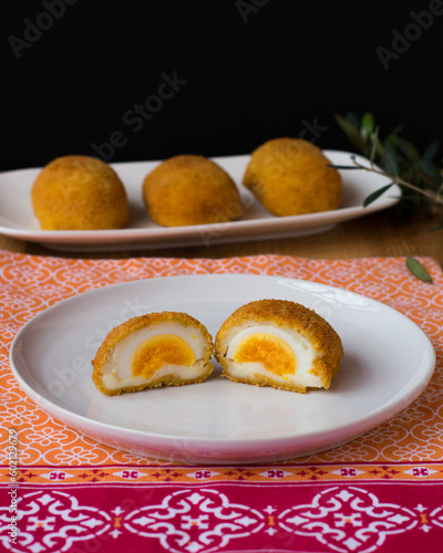 Huevos cocidos fritos servidos en plato blanco sobre mantel colorido y fondo negro. Fotografía vertical.