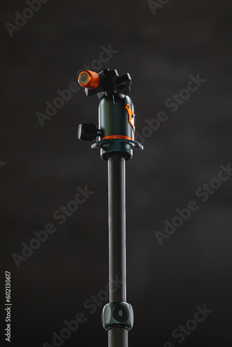 Gray central column of photo tripod with green and orange ballhead on top photo