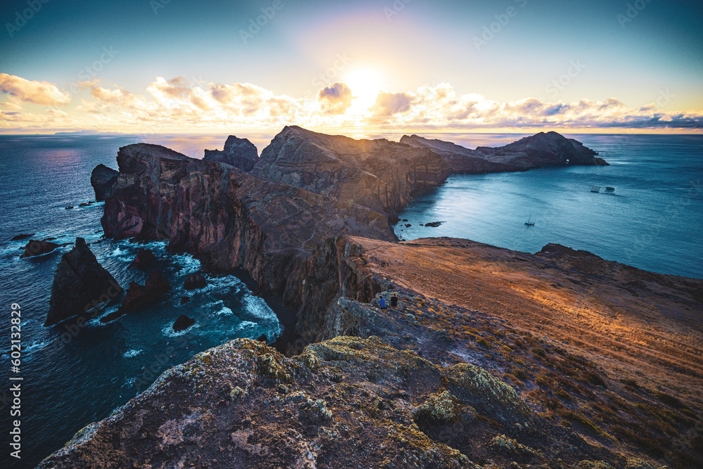 A tourist couple photographes the sunrise over the foothills of a volcanic island and the Atlantic Ocean. São Lourenço, Madeira Island, Portugal, Europe.