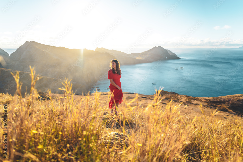 Fototapeta premium Elegant woman in red dress enjoys the morning atmosphere from the foothills of a volcanic island in the Atlantic Ocean. São Lourenço, Madeira Island, Portugal, Europe.