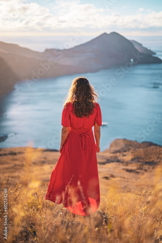 Back view of a woman in red dress standing on a rock on a volcanic island in the Atlantic Ocean in the morning. São Lourenço, Madeira Island, Portugal, Europe.