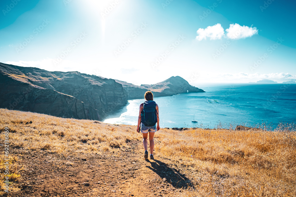 Fototapeta premium Tourist woman walking down a hill overlooking the coastal landscape of Madeira Island and the Atlantic Ocean. São Lourenço, Madeira Island, Portugal, Europe.