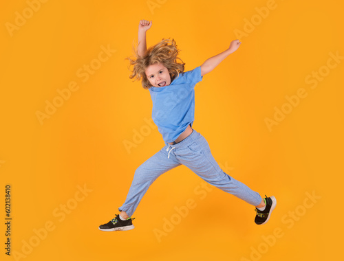 Kid boy jump fly movement wear shirt and jeans isolated on yellow studio background.