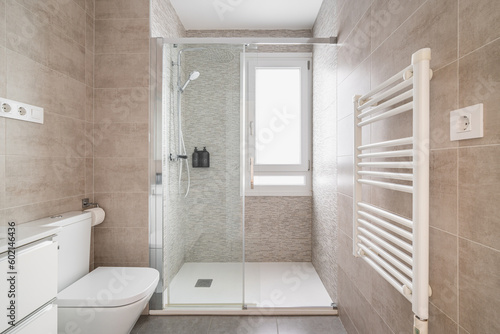 Comfortable bathroom with a toilet bowl and a shower cabin with tiles in beige tones and a window for natural light. The concept of a bathroom in a hotel or apartment after renovation