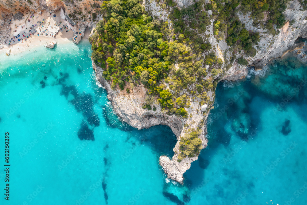 Naklejka premium Summer holiday background. Top view of seascape with beautiful coastline and small sandy beach with crowd of people on summer day. Sea coast with blue, turquoise clear water, aerial drone shot