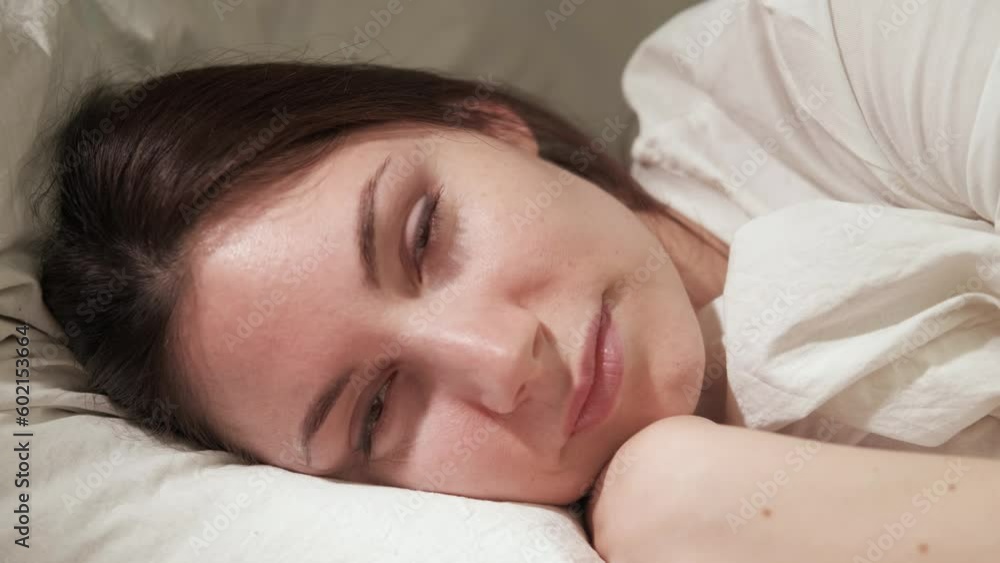 An attractive young brunette woman lies on her side on the bed, wakes up under the early morning rays and smiles An attractive young brunette woman lies on her side on the bed, wakes up under the early morning rays and smiles