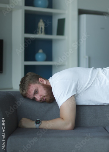 Exhausted young man fell asleep on comfortable couch in modern living room, having no energy after hard working day. Tired depressed unmotivated european guy napping on sofa at home, fatigue concept.