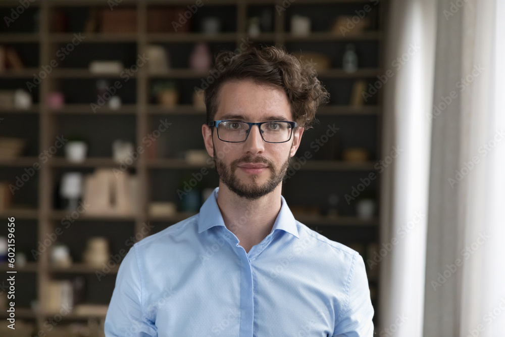 Serious Caucasian business man in stylish glasses head shot portrait. Handsome young male model with curly hair wearing trendy eyeglasses, pale blue office shirt, looking at camera Serious Caucasian business man in stylish glasses head shot portrait. Handsome young male model with curly hair wearing trendy eyeglasses, pale blue office shirt, looking at camera