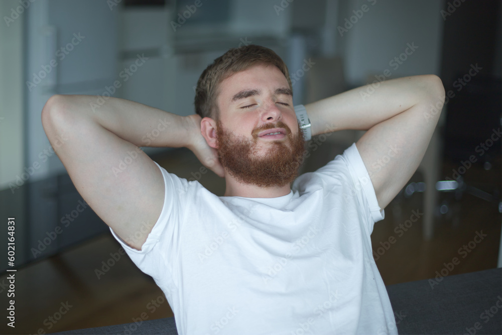 Young man with a beard alone at home, relax in living room ,sitting on the couch and meditating in the lotus position, in casual clothes Young man with a beard alone at home, relax in living room ,sitting on the couch and meditating in the lotus position, in casual clothes