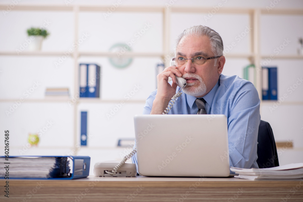 Old male employee speaking by phone in the office Old male employee speaking by phone in the office