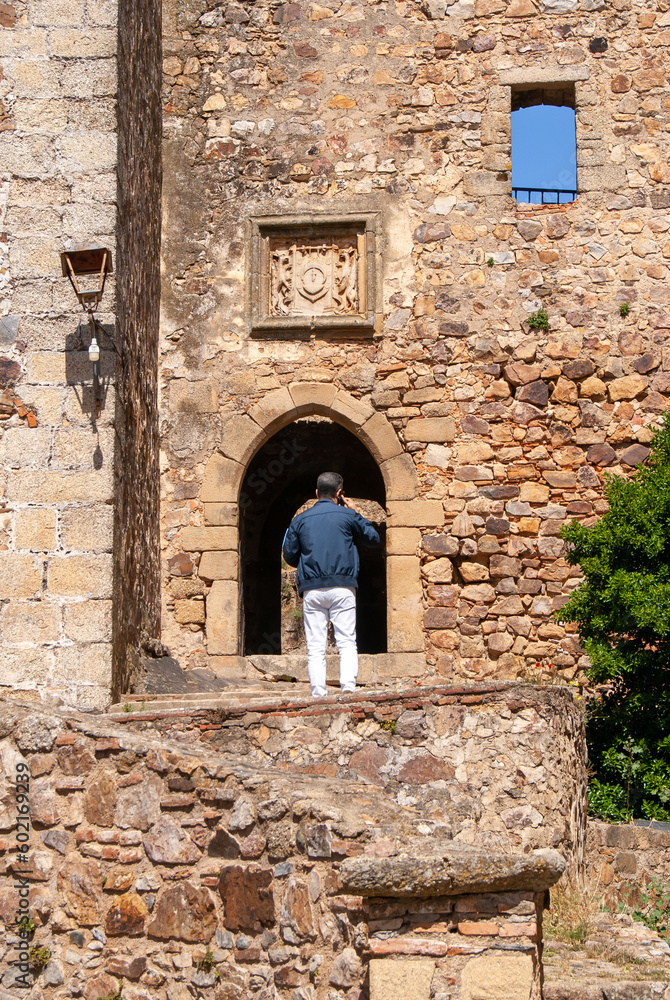 Turista hablando por teléfono delante de un pórtico de un castillo medieval.