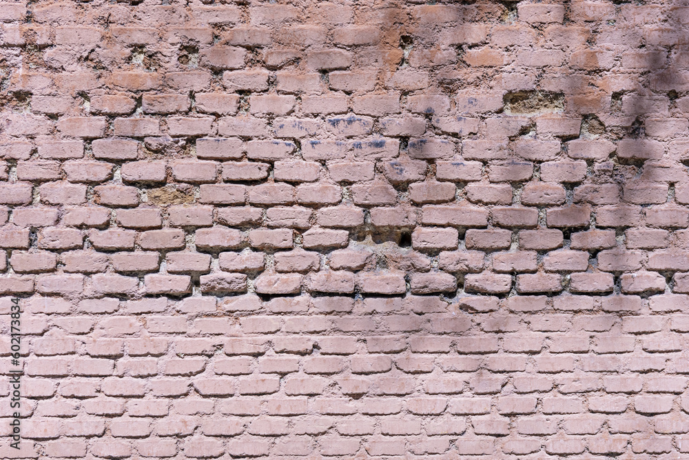 An old brick wall with deformities painted in a pale pink color An old brick wall with deformities painted in a pale pink color