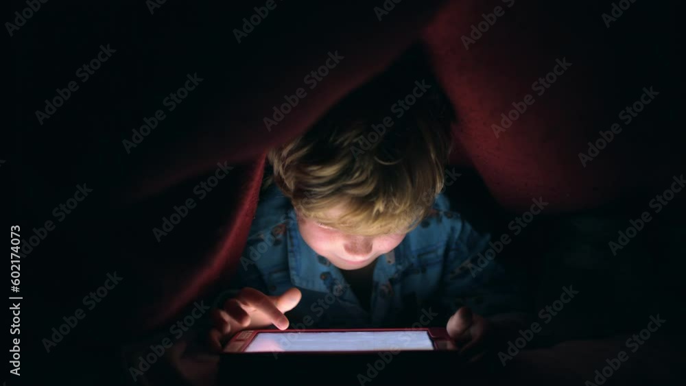 Night, light and tablet with child with blanket after bedtime for internet, movie and technology for streaming service. Relax, learning and digital with boy in bedroom hiding and playing online games Night, light and tablet with child with blanket after bedtime for internet, movie and technology for streaming service. Relax, learning and digital with boy in bedroom hiding and playing online games