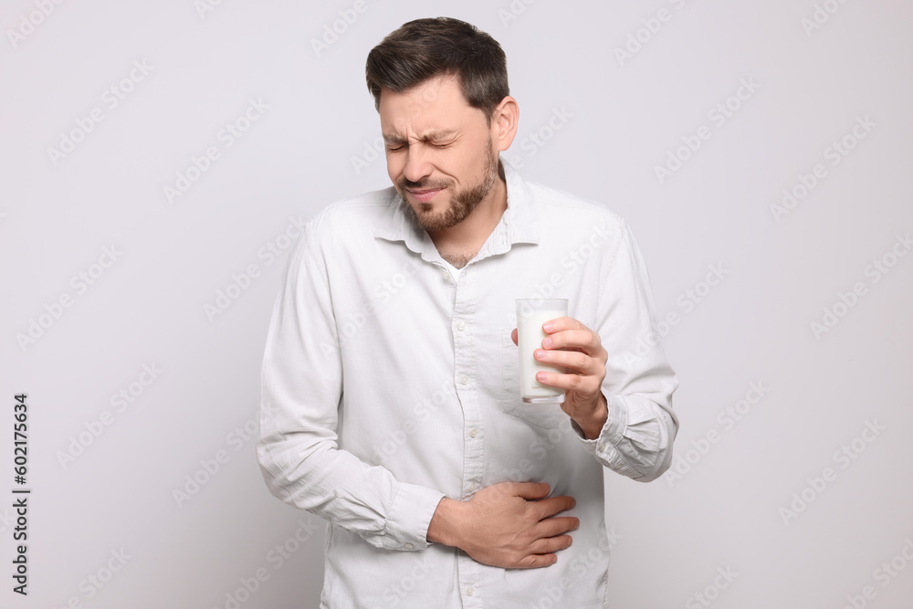 Man with glass of milk suffering from lactose intolerance on white background Man with glass of milk suffering from lactose intolerance on white background