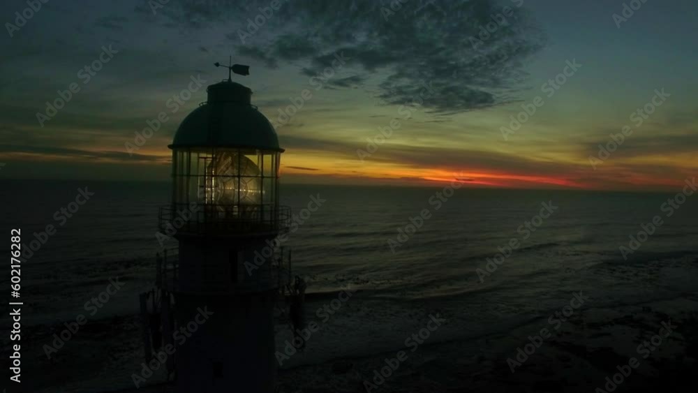 Aerial, drone and lighthouse at the ocean on a sunset sky at night or morning sunrise. Landscape of a light or spotlight at a dark beach for direction, safety or navigation and security in silhouette Aerial, drone and lighthouse at the ocean on a sunset sky at night or morning sunrise. Landscape of a light or spotlight at a dark beach for direction, safety or navigation and security in silhouette