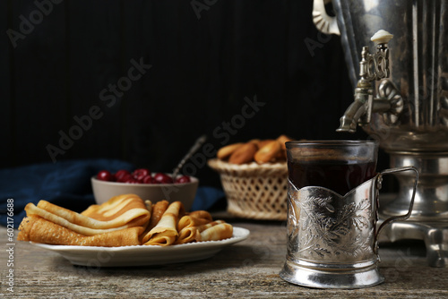 Metal samovar with cup of tea and crepes on wooden table, space for text