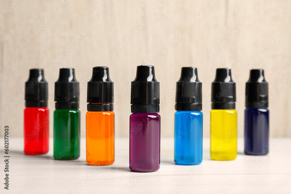 Glass bottles with different food coloring on white wooden table