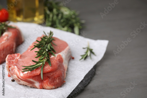 Fresh raw meat with rosemary on grey wooden table, closeup. Space for text
