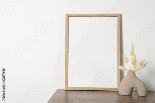 Empty photo frame and vase with dry decorative spikes on wooden table. Mockup for design