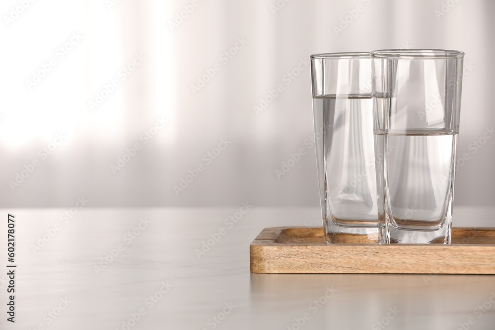 Glasses with water on white table against blurred background. Space for text - obrazy, fototapety, plakaty 