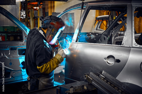 Photos Worker in mask welds metal parts of auto carcass in shop