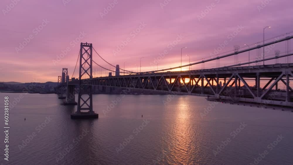 Drone flying above water surface along Bay Bridge construction with cars traffic 4K. Beautiful aerial view of Bay Bridge. Skyscrapers in downtown San Francisco at cinematic rose golden sunset light Drone flying above water surface along Bay Bridge construction with cars traffic 4K. Beautiful aerial view of Bay Bridge. Skyscrapers in downtown San Francisco at cinematic rose golden sunset light