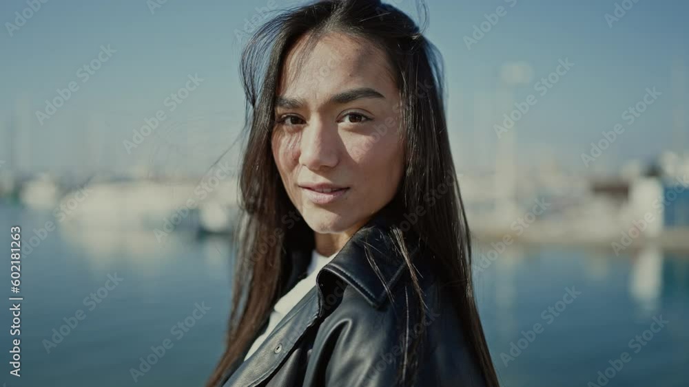 Young beautiful hispanic woman standing with serious expression combing hair with hand at seaside Young beautiful hispanic woman standing with serious expression combing hair with hand at seaside