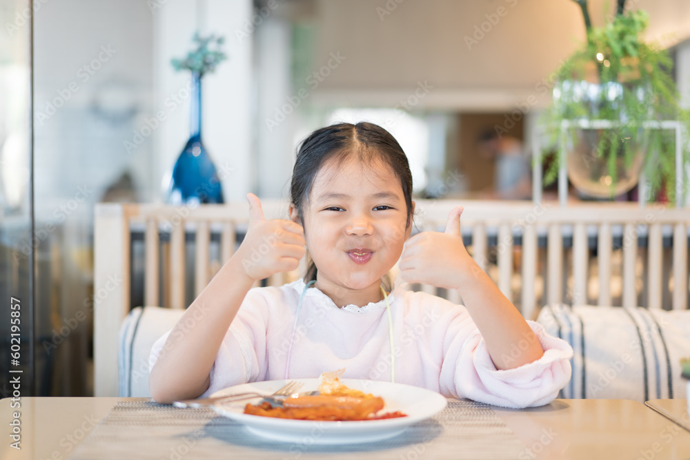 Asian child or kid girl enjoy eating breakfast by fried egg sausage bacon for morning food or cuisine to happy smile delicious and like thumb up on table in kitchen at home or restaurant with family Asian child or kid girl enjoy eating breakfast by fried egg sausage bacon for morning food or cuisine to happy smile delicious and like thumb up on table in kitchen at home or restaurant with family